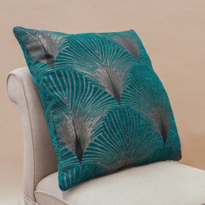 Peut inclure: Coussin bleu sarcelle avec un motif géométrique de plumes stylisées argentées et noires.