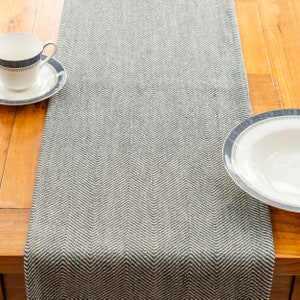 Może przedstawiać: Szary i biały bieżnik stołowy w wzór jodełki. Bieżnik jest wykonany z tkaniny tkanej i ma subtelny połysk.