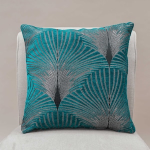 Peut inclure: Un coussin bleu sarcelle avec un motif géométrique de lignes noires et argentées. Le motif ressemble à un éventail ou à des plumes de paon.