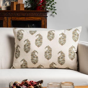 Peut inclure: Coussin rectangulaire crème avec un motif cachemire répété en vert olive, or et bleu. Le coussin est posé sur un canapé blanc, pour la décoration intérieure.