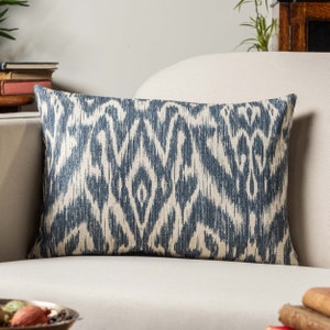 Puede incluir: Una almohada lumbar azul y blanca con un diseño ikat. La almohada está en un sofá blanco.