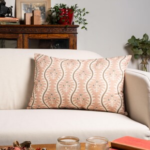 May include: Rectangular cushion featuring a repeating floral design in pink, grey, and cream. The cushion is placed on a white sofa, showcasing a classic home decor style.