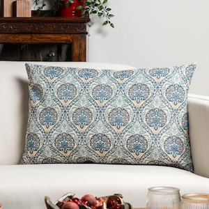 Può includere: Cuscino decorativo rettangolare con un motivo floreale blu, verde acqua e beige. Il cuscino è su un divano bianco. Il motivo presenta un design ripetuto di fiori e foglie stilizzate, creando un aspetto simmetrico e ornato. Il cuscino aggiunge un tocco di eleganza.