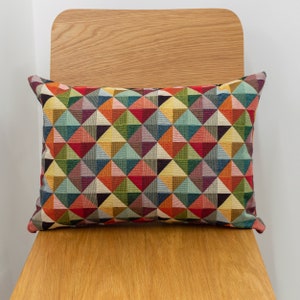 Almofada Boudoir Dupla Face com Tapeçaria Geométrica. Padrão Arlequim Triangular Multicolorido em Vermelho, Azul, Verde e Amarelo. Retângulo de 43 cm x 30 cm.