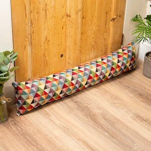 May include: A colourful doorstop with a geometric pattern in shades of red, green, blue, yellow, and purple. The doorstop is made of fabric and is shaped like a cylinder.