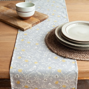Chemin de table Dainty Songbird en gris pierre délicat avec des détails jaune ocre. Conception d&#39;oiseaux et de feuilles florales. Disponible en deux tailles.