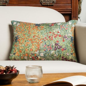 Puede incluir: Un cojín rectangular con un patrón de tapiz tejido denso que representa un prado de flores silvestres. El diseño muestra una rica variedad de pequeñas flores coloridas en tonos rojo, naranja, amarillo, morado y blanco sobre un fondo verde.