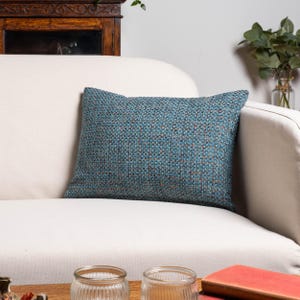 Peut inclure: Un coussin rectangulaire tissé en bleu sarcelle et marron repose sur un canapé blanc. Le coussin a un aspect texturé, avec un mélange de bleu sarcelle, de marron et d'autres couleurs tissées ensemble. C'est un article décoratif.