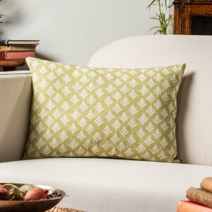 Puede incluir: Una almohada de tiro verde y blanca con un diseño de hojas. La almohada está sentada en un sofá blanco.