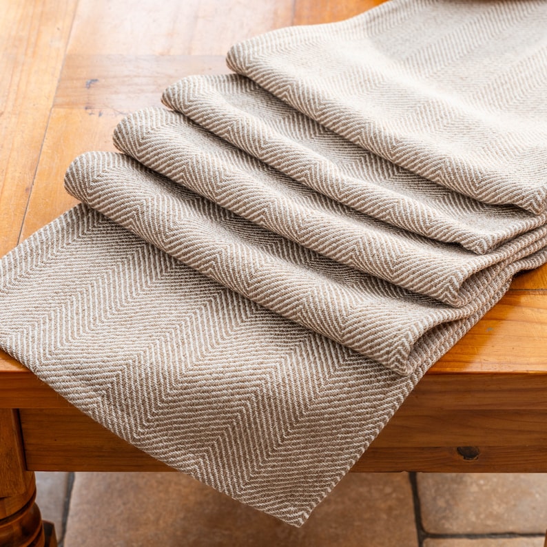 May include: A brown and white herringbone table runner. The runner is folded in thirds and is lying on a wooden table.