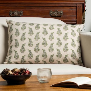 May include: A rectangular throw pillow featuring a light beige fabric base with a repeating pattern of green and grey botanical paisley-style motifs arranged in vertical columns across the entire surface of the pillow cover.
