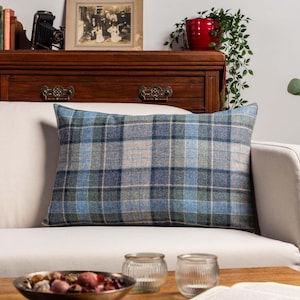 Könnte beinhalten: Ein rechteckiges Kissen mit blauem, grünem und beigem Karomuster liegt auf einem weißen Sofa. Das Karomuster des Kissens verleiht der Raumdekoration einen klassischen, traditionellen Touch.