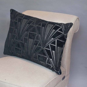 Peut inclure: Un coussin de décoration noir et argent à motif géométrique avec un léger brillant. Le coussin est posé sur un fauteuil beige clair.