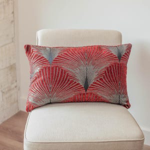 Peut inclure: Un coussin rectangulaire décoratif avec un fond rouge et un motif argenté en forme d'éventail. Le coussin est posé sur une chaise beige, présentant un design moderne pour la décoration intérieure.