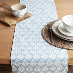May include: A blue and white patterned table runner with a woven jute placemat and white bowls.