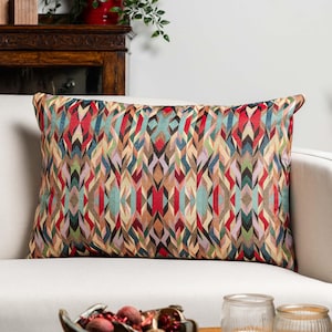May include: A rectangular cushion with a colourful geometric design in red, blue, green, and brown. The cushion is placed on a white sofa. The pattern features repeating diamond and arrow shapes, creating a vibrant, textured appearance.