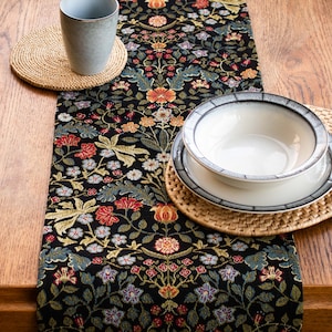 May include: A black and gold floral table runner with a woven placemat and a white bowl with a grey rim.