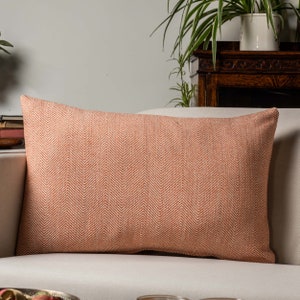 Op de afbeelding: Een rechthoekig oranje en wit kussen met een herringbone-patroon. Het kussen ligt op een witte bank.