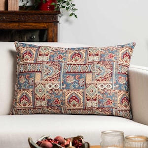 Puede incluir: Cojín rectangular con diseño de patchwork. El cojín presenta un patrón de cuadrados en tonos azul, rojo, beige y crema. El cojín está sobre un sofá blanco.