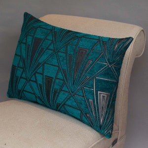 Può includere: Cuscino da lancio color turchese e nero con un motivo geometrico di design art déco moderno. Il cuscino è seduto su una sedia beige.
