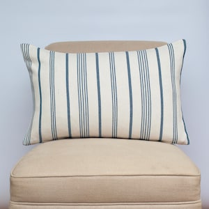 Peut inclure: Un coussin lombaire rayé blanc et turquoise sur un fauteuil beige. Le coussin est fait d'un tissu doux et tissé.