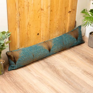 May include: A long, rectangular doorstop with a teal and gold fan-shaped pattern. The doorstop is resting on a light wood floor in front of a wooden door. The doorstop is approximately 91 cm long.