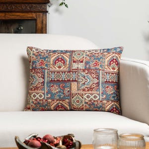 Op de afbeelding: Rechthoekig kussen met een patchwork ontwerp. Het kussen heeft een patroon van vierkanten in tinten blauw, rood, beige en goud. Het ontwerp bevat bloemen- en paisley-motieven, waardoor een decoratief accent ontstaat.