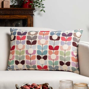 Op de afbeelding: Rechthoekig decoratief kussen met een bloemenpatroon in diverse kleuren, waaronder rood, blauw, paars en groen. Het kussen ligt op een witte bank. Het bloemmotief is een herhalend patroon.