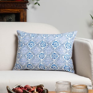 May include: A rectangular cushion with a blue and white floral pattern. The cushion is placed on a white sofa. The pattern features stylized flowers and geometric shapes, creating a visually appealing design.