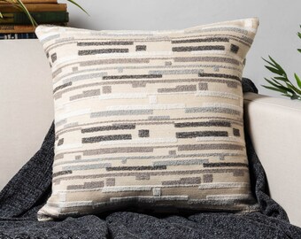 May include: A beige throw pillow with a geometric pattern in shades of gray and brown. The pillow is made of a soft, textured fabric and has a subtle sheen.