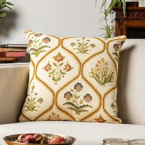 Könnte beinhalten: Ein cremefarbenes Kissen mit einem Blumenmuster. Das Muster zeigt rote, orange, gelbe und grüne Blumen auf cremefarbenem Hintergrund. Das Kissen ist aus einem weichen, gewebten Stoff.