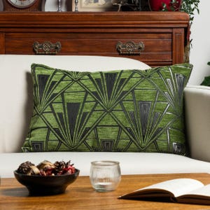 Può includere: Un cuscino rettangolare con una base in tessuto verde brillante e un motivo geometrico ripetitivo in nero e argento. Il design è composto da linee angolari nette e forme a ventaglio che creano un effetto visivo strutturato e simmetrico.