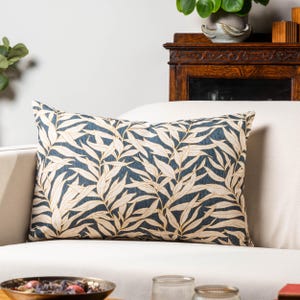 May include: A decorative throw pillow with a blue background and a white leaf pattern. The pillow is sitting on a white couch.