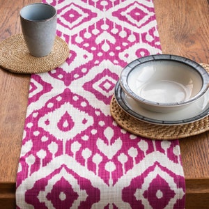 Pode incluir: Um corredor de mesa estampado em rosa e branco com um tapete de lugar tecido e uma tigela branca com borda cinza em cima.