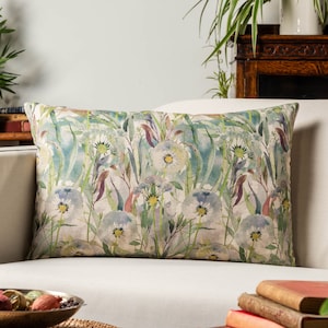 Può includere: Un cuscino rettangolare con un motivo floreale. Il cuscino presenta un design in stile acquerello di fiori bianchi con foglie e steli verdi su uno sfondo beige chiaro.