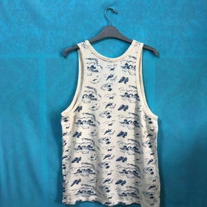 May include: A white sleeveless shirt with a blue and white print of clouds and airplanes. The shirt is hanging on a black hanger against a blue background.