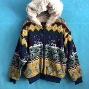 Pode incluir: Uma jaqueta de malha com padrão azul, amarelo, verde e vermelho com capuz forrado de pele sintética branca. A jaqueta tem um fecho de correr.