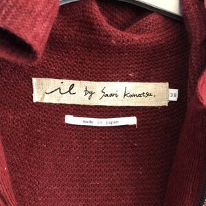 Puede incluir: Un c&aacute;rdigan de punto color burdeos con cierre de cremallera. La etiqueta dice "il by Saori Komatsu." y "made in japan."