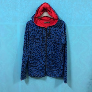 May include: Blue and black leopard print zip-up hoodie with a red hood. The hoodie has the text "Hell Cat Punks" printed on the front.