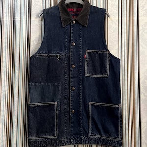 Può includere: Un giubbotto di jeans blu scuro con colletto in velluto a coste e diverse tasche. Il giubbotto ha una chiusura con bottoni e la parola "KAPITAL" è visibile sul colletto.