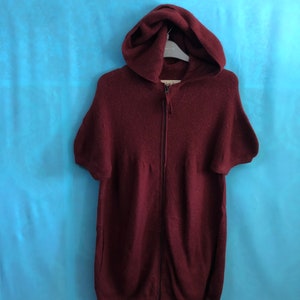 Puede incluir: Una sudadera con capucha color burdeos con cierre de cremallera y mangas cortas.