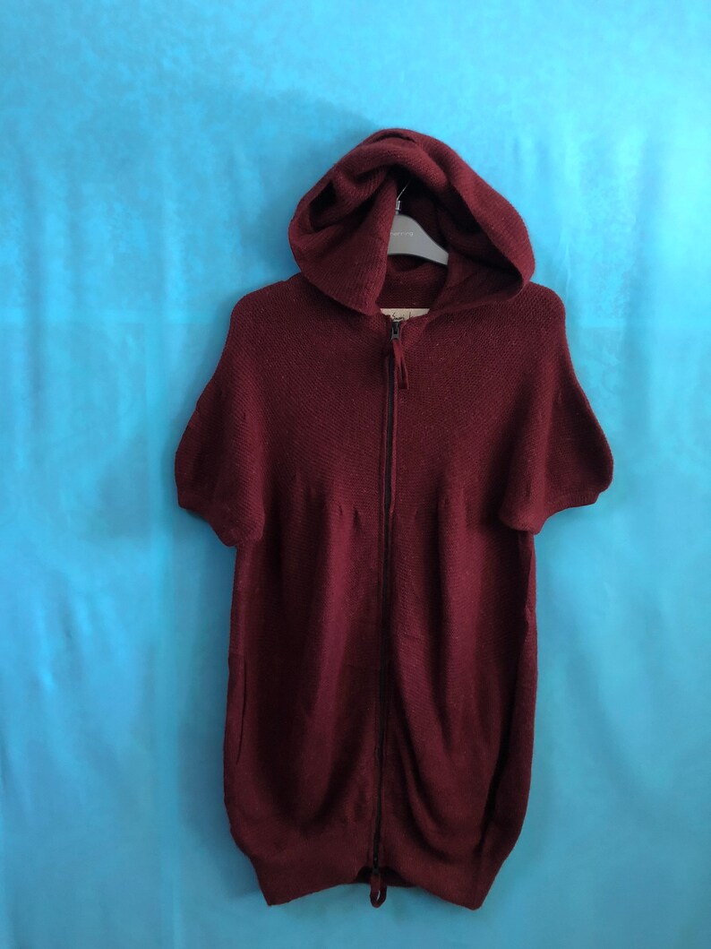 Puede incluir: Una sudadera con capucha color burdeos con cierre de cremallera y mangas cortas.