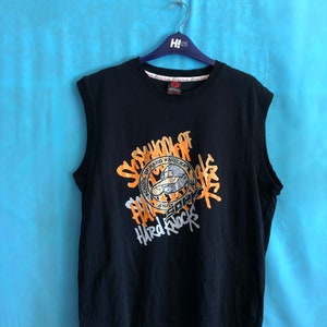 Könnte beinhalten: Schwarzes ärmelloses Shirt mit einem grafischen Aufdruck eines Comic-Charakters mit Hut und Sonnenbrille. Der Aufdruck enthält den Text "School of Hard Knocks" und "Hard Rock".