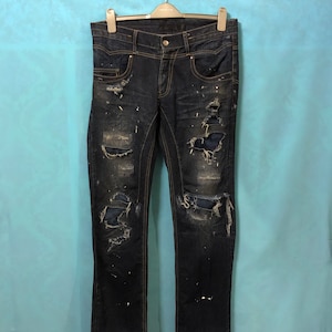 Op de afbeelding: Donkerblauwe denim jeans met distressed details, waaronder scheuren, gaten en verfspatten. De jeans hebben een slanke pasvorm en een rechte pijp.