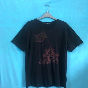 May include: A black t-shirt with a red embroidered design of a flag with a heart and a group of figures.