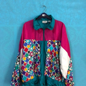 May include: A retro zip-up jacket in a striking colour block design. The jacket has a magenta upper, teal collar and trim, and a geometric pattern in the centre with white and teal accents. The jacket is hanging on a silver hanger.