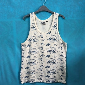 May include: A white tank top with a blue and white print of islands and airplanes. The tank top has a scoop neck and a relaxed fit. The brand name "PX" is printed on the front of the tank top.