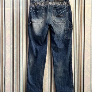 May include: Blue denim jeans with distressed detailing and a black waistband with the text "UBUSUPERGANG" in white.
