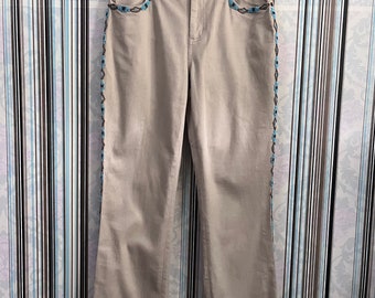 May include: Beige straight-leg jeans with blue and brown embroidery along the sides. The jeans have a zipper fly and belt loops.