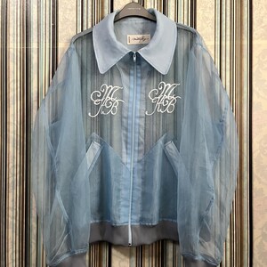 May include: A light blue sheer jacket with a zipper closure and embroidered initials on the front. The jacket has a collared neckline and a ribbed hem.